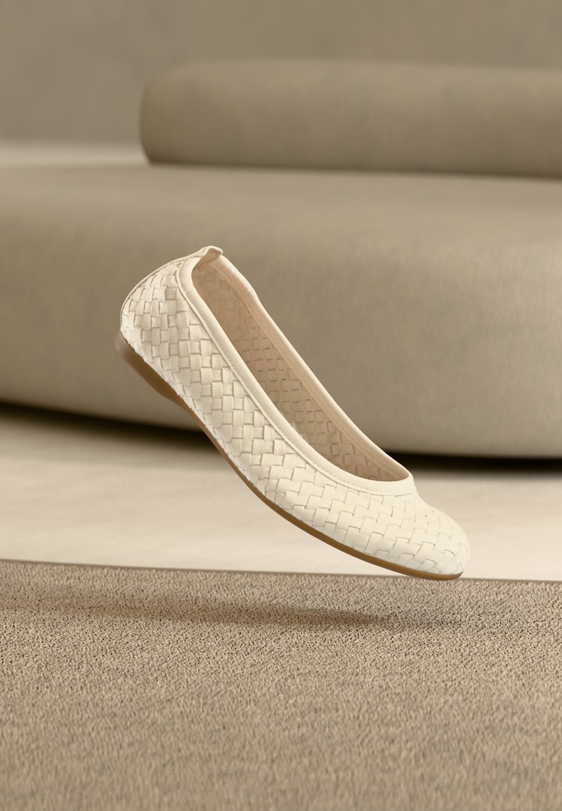 Λευκό υφαντό δερμάτινο μπαλαρίνα παπούτσι με στρογγυλή μύτη και λεπτή σόλα, αιωρούμενο πάνω από μια υφασμάτινη, σε ουδέτερους τόνους επιφάνεια. Μαλακό, εύκαμπτο υλικό.