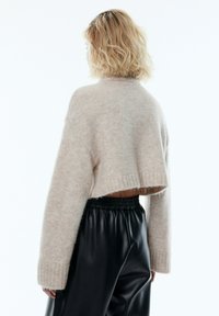 Helles beige, kurzes Sweatshirt aus weichem, flauschigem Material mit weiten Ärmeln und gerippten Bündchen, kombiniert mit schwarzen Lederhosen.
