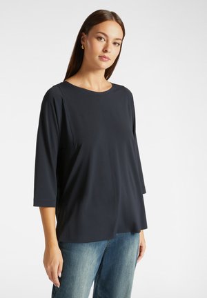 Top blu navy con scollatura rotonda e maniche a tre quarti. Realizzato in tessuto morbido, presenta una cucitura centrale e una vestibilità rilassata.