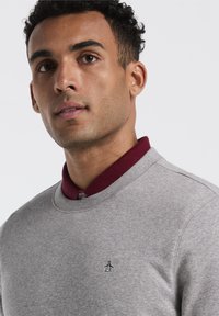 Lichtgrijze sweatshirt met een bordeauxrode kraag. Bevat een klein geborduurd pinguïnlogo op de borst. Zacht, gestructureerd materiaal.