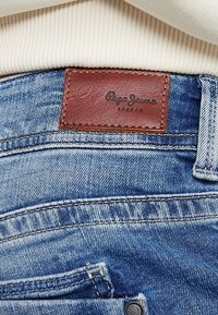 Blå denimjeans med framträdande sömmar och en brun läderetikett med "Pepe Jeans London" präglad på.