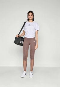 Adidas siva torba za teretanu, bijela majica i smeđi tajice. Tajice imaju dizajn s blokovima boja; cipele su bijele s crnim detaljima.