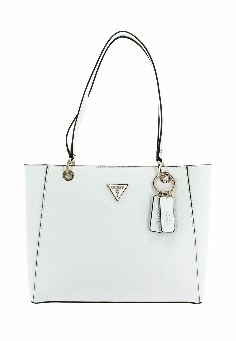 Sac cabas blanc Guess avec poignées doubles bordées de noir, logo triangle doré et deux étiquettes pendantes, dont une embossée "1981".
