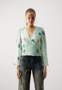 Bluza u mint zelenoj boji s cvjetnim uzorkom, dugim napuhanim rukavima i smokanim strukom, s dubokim V-izrezom i delikatnim detaljima od dugmadi.