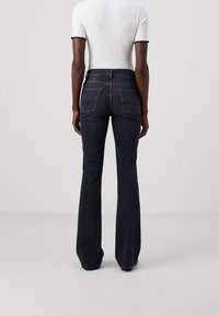 Jeans évasés bleu marine, avec des poches arrière et des détails de couture subtils, associés à un haut ajusté à côtes blanches avec des bordures noires.