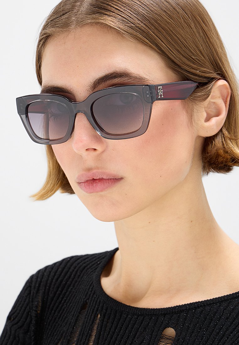 Sonnenbrillen mit quadratischer Form, dunkelgrauen Rahmen und getönten Gläsern. Mit roten Akzenten an den Bügeln und einem dezenten Logodetail.