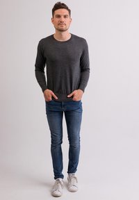 Maglietta grigia scuro a maniche lunghe, jeans blu slim-fit e sneakers bianche. Il tessuto sembra liscio; il design è semplice, senza motivi o dettagli.