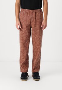 Brown patterned jogger pants with an elastic waistband, featuring a subtle design throughout and a straight cut. Paired with dark sneakers.