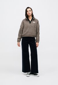 Brązowy polar z półzamkiem i logo "GAP", zestawiony z ciemnymi, szerokimi spodniami sztruksowymi oraz czarnymi trampkami z białymi podeszwami.