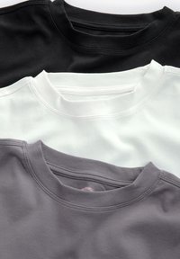 Drei Crewneck-T-Shirts übereinander gestapelt: schwarz, weiß und grau. Jedes hat gerippte Ausschnitte und eine weiche Stofftextur; einfache und einfarbige Designs.