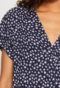 Vestido navy con escote en V que presenta un patrón floral blanco. Mangas cortas y tejido suave, ideal para un look casual.