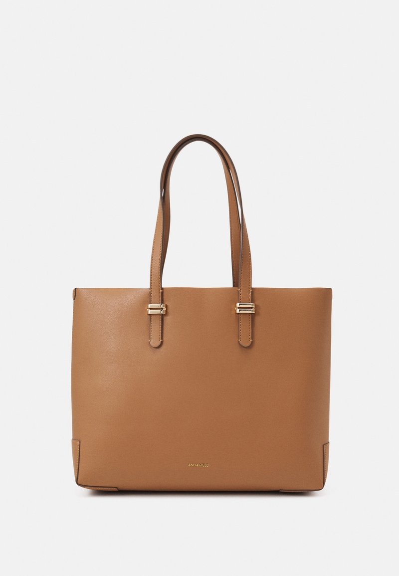 Sac fourre-tout en cuir marron avec deux bandoulières et des détails de boucles dorées, arborant le logo "ANNA FIELD" au centre à l'avant.