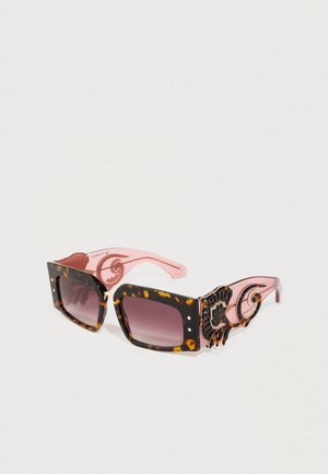 Lunettes de soleil carrées écaille de tortue avec des branches roses ornées de tourbillon noir et des verres dégradés foncés sur fond blanc.