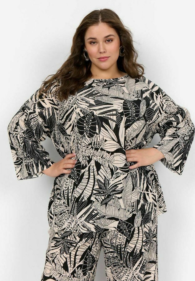 Zwart en beige top met botanische print, met brede mouwen en een losse pasvorm, gedragen over bijpassende broek met een vergelijkbaar patroon.