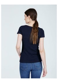 Granatowa dopasowana koszulka z krótkimi rękawami i okrągłym dekoltem, zestawiona z niebieskimi dżinsami z tylnymi kieszeniami.