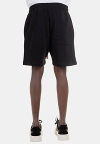 Shorts neri in cotone con una vita elastica, dotati di una tasca laterale e una vestibilità rilassata, indossati con sneakers bianche e nere.