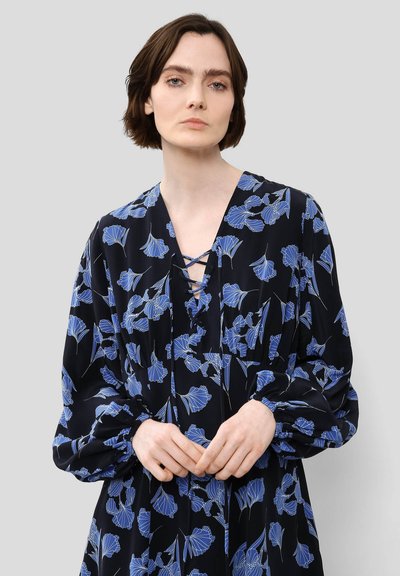 Μαύρο φόρεμα με μπλε λουλουδάτο σχέδιο, ντεκολτέ σε σχήμα V με λεπτομέρεια σε κεντημένα κορδόνια, μακρυά φουσκωτά μανίκια και άνετη εφαρμογή. Λείος υφασμάτινος χαρακτήρας.