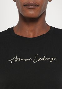 Zwarte katoenen T-shirt met een witte geborduurde "Armani Exchange" logo in cursief. Klassiek crewneck ontwerp, zachte textuur.