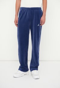 Sötétkék melegítőnadrág puha anyagból, fehér oldalsó csíkkal és egy kis logóval. Kényelmes elasztikus derékrész.