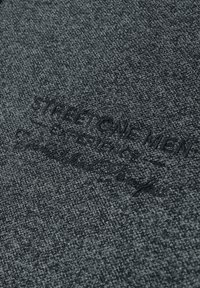 Grauer Stoff mit einer strukturierten Strickqualität. Verfügt über geprägten Text mit der Aufschrift "STREET ONE MEN" und zusätzliche Branding-Details.