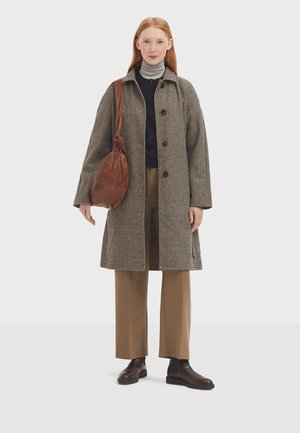 Brown checked coat with large buttons, beige turtleneck, brown trousers, and dark brown boots. Brown bag with a knotted strap.