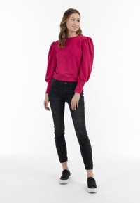 Jersey fucsia con mangas abullonadas, ajustado en la cintura. Combinado con jeans negros ajustados y zapatos negros con suelas blancas.