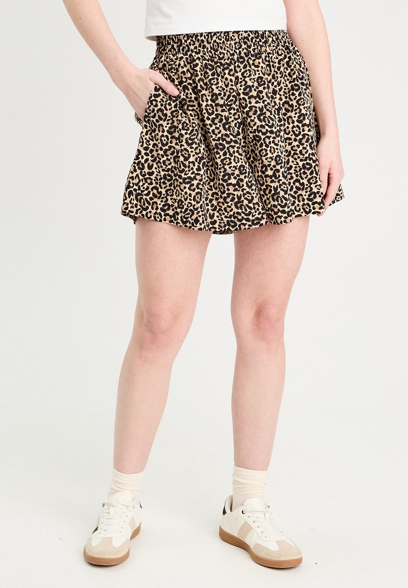 Shorts à imprimé léopard avec une ceinture élastique noire, un design évasé et des poches latérales. Portés avec des baskets blanches et des chaussettes crème.