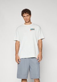 Hvid bomulds t-shirt med korte ærmer og et farverigt "NIKE" logo på brystet, sammen med grå shorts med et tekstureret mønster.