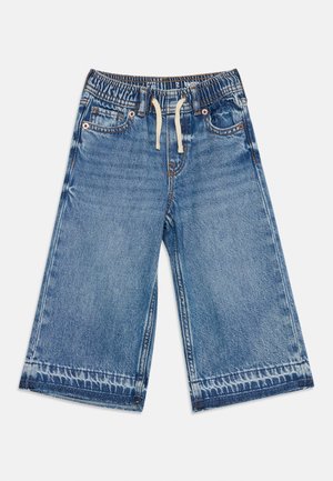 Short large en denim bleu avec taille élastique et cordon blanc, comprenant des poches avant et des détails délavés aux ourlets.