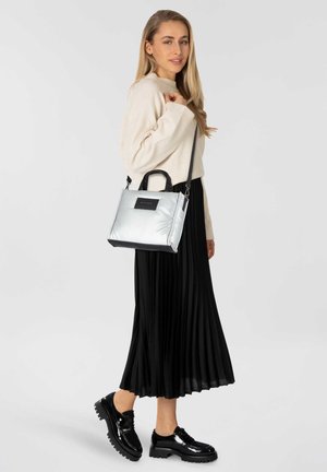 Bolso de mano plateado con acentos negros, diseño cuadrado, textura suave, doble asa y correa de hombro ajustable.