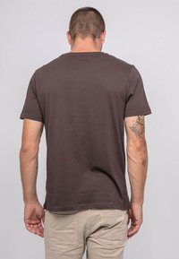 T-shirt à manches courtes marron foncé avec un col rond, présenté de dos. Il présente une texture lisse et une coupe décontractée.
