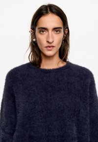 Granatowy, włochaty sweter dzianinowy z okrągłym dekoltem. Posiada miękką strukturę oraz długie rękawy, zapewniając luźny krój.
