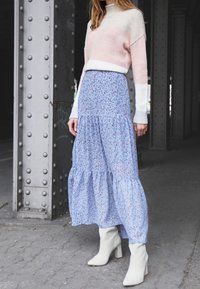 Pull en tricot rayé rose clair et crème avec un col montant, associé à une jupe maxi bleue à fleurs et des bottines blanches, dans un cadre urbain.