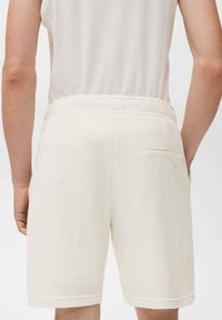 Shorts blancs texturés avec une coupe décontractée. Comprend une poche arrière et une taille élastique. Le tissu lisse offre une sensation légère et respirante.