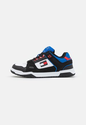 Schwarz-weißer Sneaker mit blauen und roten Akzenten, gepolstertem Kragen, mehreren Texturen und einem rechteckigen Logo an der Seite.
