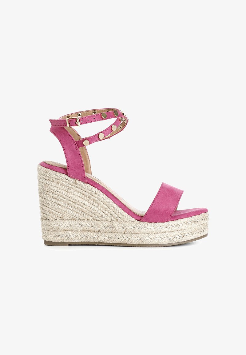 Sandale compensée en espadrille rose avec une base en jute, bride de cheville ornée de clous dorés et design à bout ouvert. Texture en daim lisse.