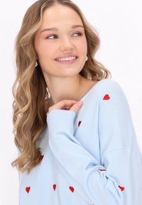 Maglione azzurro chiaro con maniche lunghe, caratterizzato da motivi a cuore rossi e polsini a coste. Morbido al tatto e vestibilità comoda.