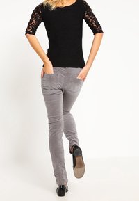 Svart spetsblus med trekvartslånga ärmar, ihopparad med grå kordflortsbyxor. Byxorna har två bakfickor och en smal passform.