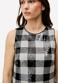 Haut sans manches à sequins noirs et blancs avec un motif à carreaux, col rond et texture lisse, réfléchissant la lumière de manière dynamique.