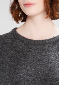 Maglione a maglia grigio scuro con scollo rotondo e un motivo testurizzato. Il tessuto sembra morbido e spesso, adatto per il clima più freddo.