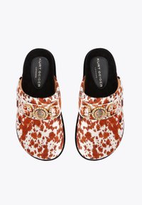 Brown and white spotted mules with a black interior, featuring a gold decorative buckle and textured plush material.