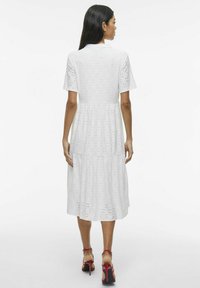 Robe en coton blanche avec des motifs en œillets, manches courtes et une jupe à volants, dotée d'un col à boutons et d'une coupe décontractée.