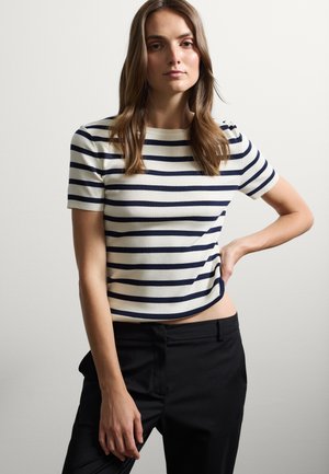 Top de punto a rayas en crema y marino, con mangas cortas, cuello redondo y un diseño ajustado, combinado con pantalones negros.