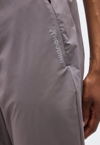 Κοντινή λήψη γκρι παντελονιού μάρκας Houdini με ένα χέρι που ακουμπά δίπλα στην πλαϊνή τσέπη.