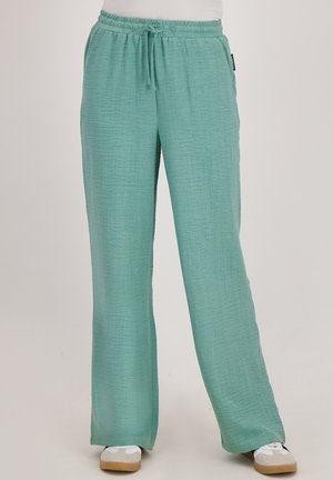 Losse zeegroen broek met een trekkoord in de taille, gedragen met witte sneakers op een effen achtergrond.