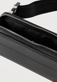 Μαύρη υφή δερμάτινη τσάντα χιαστί με ασημί φερμουάρ που είναι μισάνοιχτο, αποκαλύπτοντας μαύρο ύφασμα στο εσωτερικό και ρυθμιζόμενο λουρί.