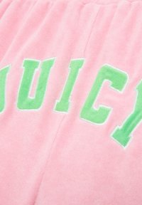 Tissu en peluche rose avec de grandes lettres vertes brodées épelant "JUICY". La texture est douce avec une finition lisse.