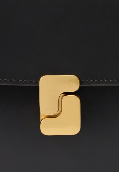 Black leather handbag with a polished gold geometric clasp. Smooth texture and discreet stitching detail along the edge.