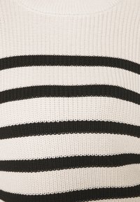 Pull tricoté avec un tissu texturé présentant des rayures horizontales en noir et blanc alternées. Encolure ronde et coupe décontractée.