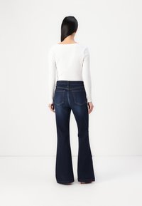 Jeans svasati blu scuro in denim, con vita alta, due tasche posteriori e orli rifiniti. Abbinati a un top bianco a coste.